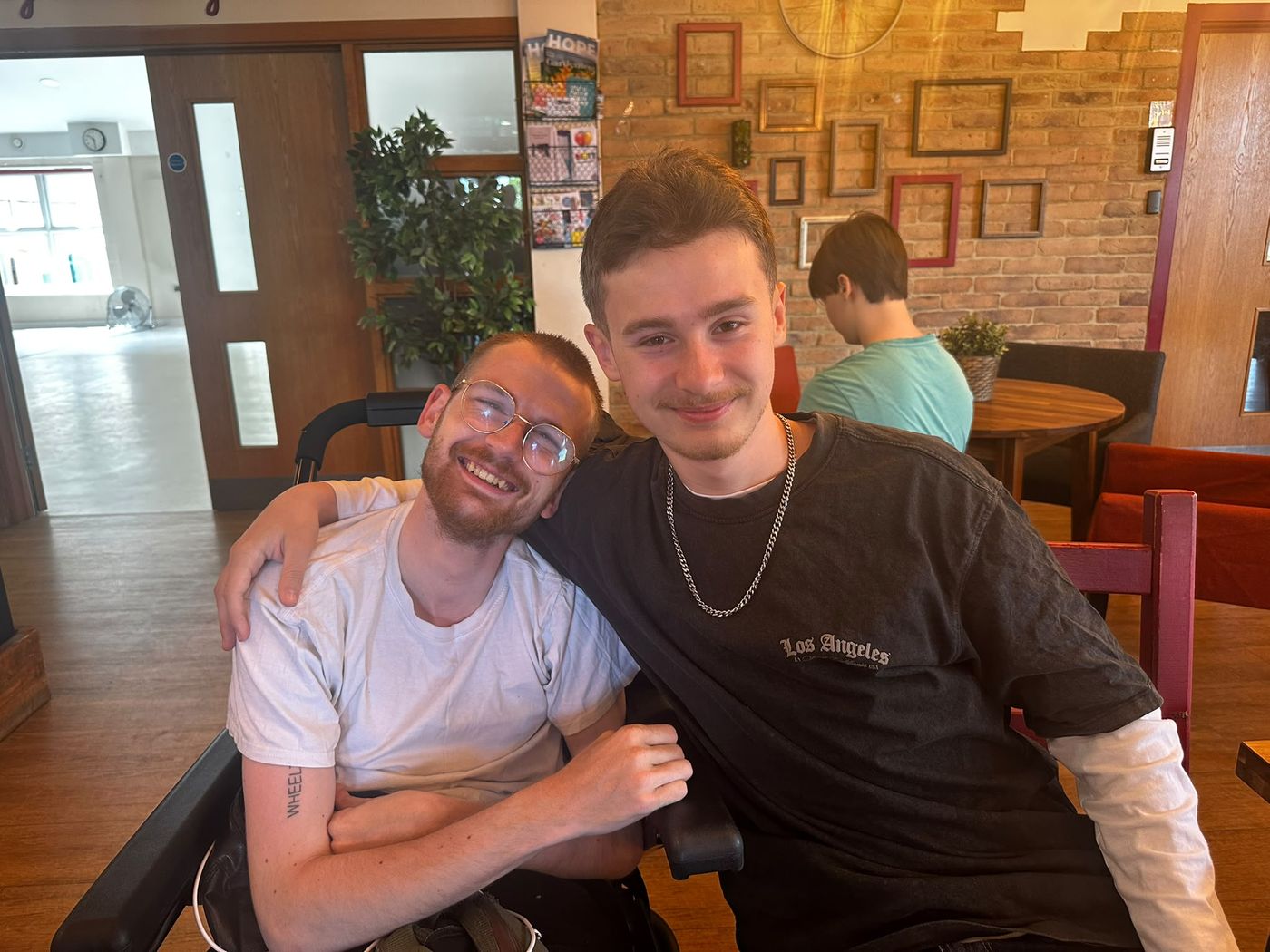 Tom and his brother grinning at a café table, his brother's arm round his shoulders.