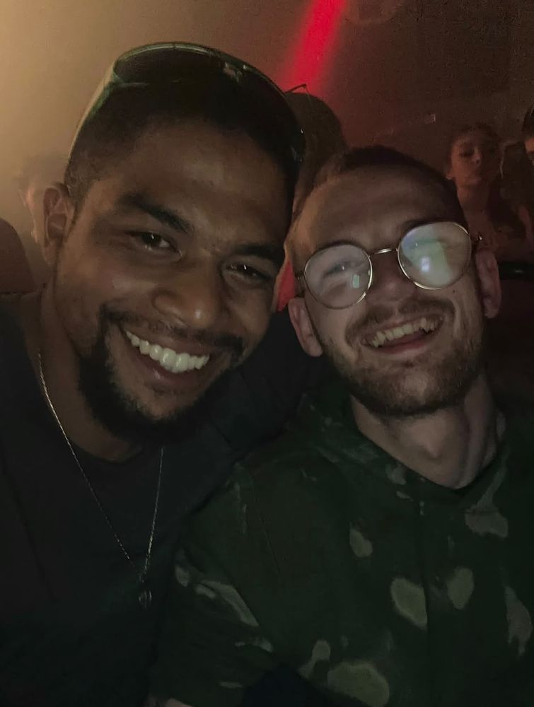 A close up selfie of Tom and a mate in a dark club, both smiling at the camera.